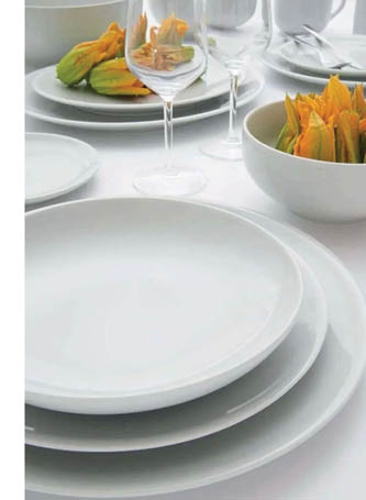 A close-up view of a white plate on a white tablecloth with part of a glass and another dish visible in the background. Description generated by AI