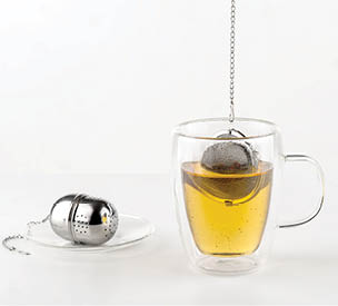 A glass cup filled with tea has a metal tea infuser suspended inside it, while another infuser rests on a small plate beside the cup. Description generated by AI