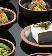 Three black bowls with a pink rim are arranged on a reflective black surface, with one bowl containing a serving of rice topped with crispy fried onions. Description generated by AI