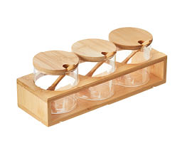 Three clear glass jars with wooden lids and spoons are neatly arranged in a rectangular wooden holder. Description generated by AI