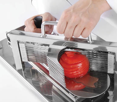 Hands are using a stainless steel slicer to cut a tomato into thin, even slices. Description generated by AI