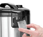 A hand is holding a transparent measuring cup next to a stainless steel and black electric appliance. Description generated by AI